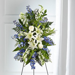 Tall standing floral spray with white lilies and blue flowers on an easel