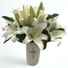 White lilies arranged in a tall vase with dark green leaves