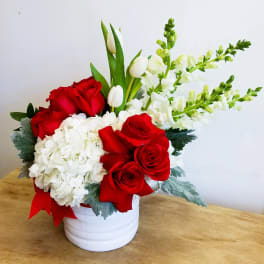 Red roses and white hydrangeas in a white vase with tulips and snapdragons