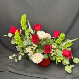 Red roses and pale ranunculus arranged in a red vase