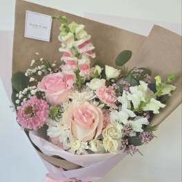 Hand-tied bouquet of pink and white flowers wrapped in brown paper
