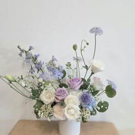 Pastel bouquet of lavender, white, and blue flowers in a white vase