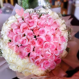 Large round bouquet of pink roses encircled by white roses in pastel wrapping paper
