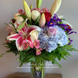 Mixed bouquet of lilies, roses, hydrangeas, and irises in a tall clear glass vase