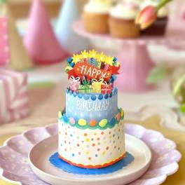 Tiered birthday cake with colorful decorations and a "Happy Birthday" topper