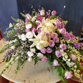 Large pastel floral arrangement with lilies, roses, and hydrangeas on a round table