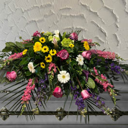 Casket spray with pink roses, yellow daisies, and purple flowers