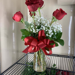 Three red roses in a glass vase with white baby's breath and a red ribbon