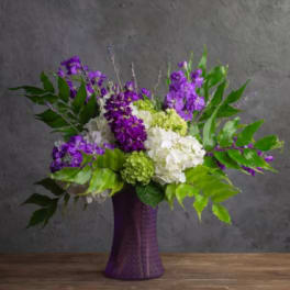 Purple and white floral arrangement in a tall purple vase