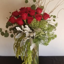 Red roses in a glass vase with green filler and silver foliage