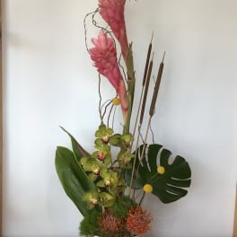 Tall tropical arrangement with pink blooms and green orchids in a white vase