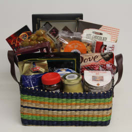 Colorful woven gift basket filled with assorted gourmet snacks, jars, and chocolate packages