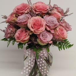 Vase arrangement of pink and lavender roses with filler blooms and a polka dot ribbon.
