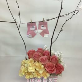 Pink roses and yellow flowers in a baby-themed box with tiny socks on branches