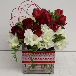 Low red and white flower arrangement with roses and hydrangeas in a square glass vase wrapped with red lace ribbon