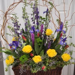 Tall floral arrangement with yellow roses and purple irises in a wicker basket