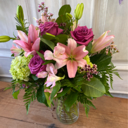 Pink lilies and purple roses arranged in a clear glass vase