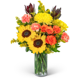 Bouquet of sunflowers, orange roses, and pink carnations in a glass vase