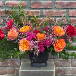 Arrangement of orange, pink, and red roses in a black vase
