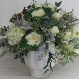 White floral arrangement in a white vase with trailing greenery