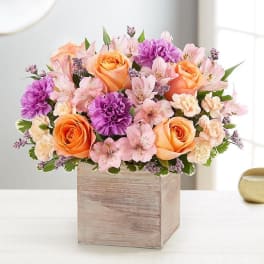 Peach roses and pink flowers arranged in a wooden box