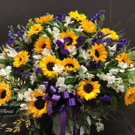 Large bouquet of sunflowers, white flowers, and purple blooms with a ribbon