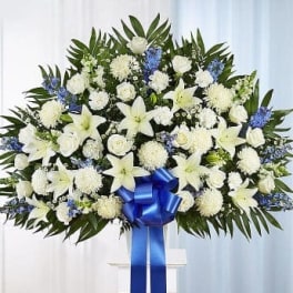 White floral standing spray with blue accents and a blue ribbon