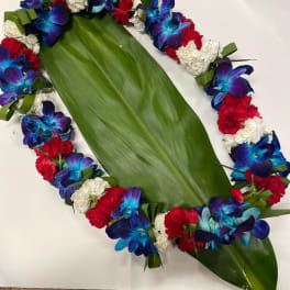 Floral lei with blue orchids, red carnations, and white flowers on a large green leaf