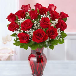 Red roses arranged in a red glass vase with white filler flowers