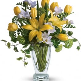 Yellow tulips and white flowers arranged in a clear glass vase