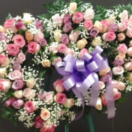 Heart-shaped wreath of pink and cream roses with a purple bow