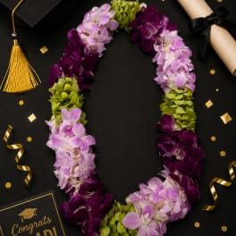 Purple and lavender orchid lei with green accents beside a graduation cap and diploma