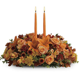 Orange floral centerpiece with two lit taper candles