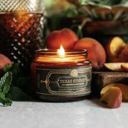 Lit candle in a glass jar surrounded by peaches and fruit slices