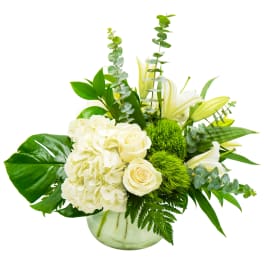 White roses and hydrangeas in a glass vase with green foliage