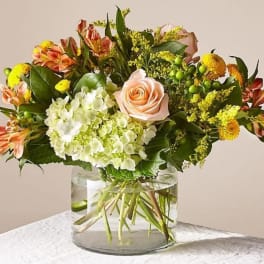 Mixed bouquet with a peach rose, hydrangea, and orange alstroemeria in a glass vase