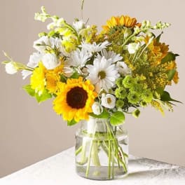 Bouquet of sunflowers, white daisies, and yellow flowers in a glass vase
