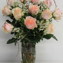 Tall glass vase of pale peach roses with small white accent flowers