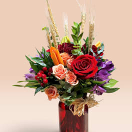 Mixed bouquet of red, peach, and purple flowers in a red glass vase