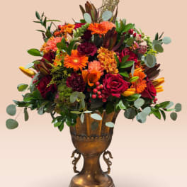 Mixed bouquet of orange, red, and pink flowers in a bronze urn vase