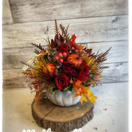Autumn floral arrangement in a white pumpkin container with red roses and fall leaves