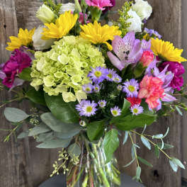 Mixed bouquet of yellow sunflowers, green hydrangea, pink carnations and asters in a clear glass vase