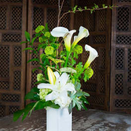 Tall white floral arrangement with calla lilies and lilies in a white vase