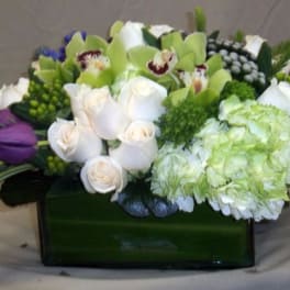 Mixed bouquet with white roses, green orchids, and purple tulips in a rectangular vase