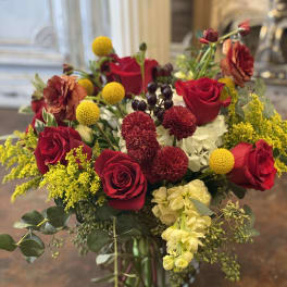 Bouquet of red roses, yellow billy balls, and mixed blooms in a glass vase