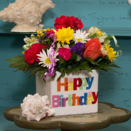 Colorful mixed flower arrangement in a white Happy Birthday container