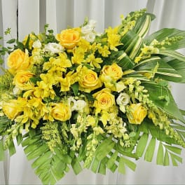 Yellow roses and mixed yellow-white flowers in a large arrangement with broad green leaves.