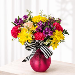 Bright mixed bouquet in a pink vase with a striped ribbon