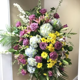 Standing floral spray with purple roses, lilies, hydrangeas, and yellow daisies