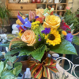 Colorful bouquet of roses, sunflowers, and iris in a vase with a ribbon